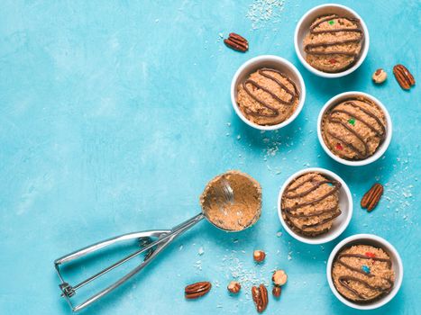 Safe-to-eat raw monster cookie dough in small portion bowl, ice cream scoop and nuts on blue background. Ideas and recipes for kids and toddlers meal. Top view or flat-lay. Copy space for text.