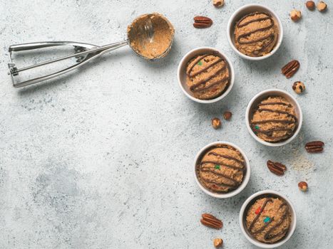 Safe-to-eat raw monster cookie dough in small portion bowl, ice cream scoop and nuts on gray cement background. Ideas and recipes for kids and toddlers meal. Top view or flat-lay. Copy space for text.