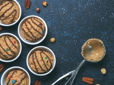 Safe-to-eat raw monster cookie dough in small portion bowl, ice cream scoop and nuts on dark blue background. Ideas and recipes for kids and toddlers meal. Top view or flat-lay. Copy space for text.