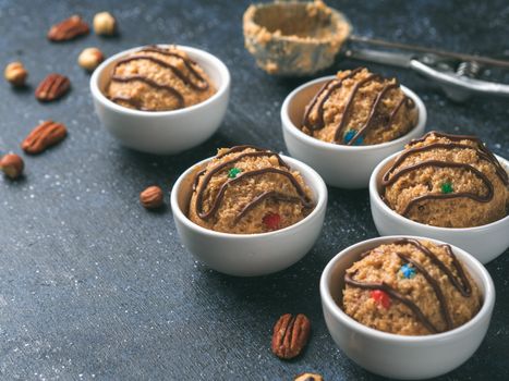 Safe-to-eat raw monster cookie dough in small portion bowl, ice cream scoop and nuts on dark blue background. Ideas and recipes for kids and toddlers meal. Copy space for text.