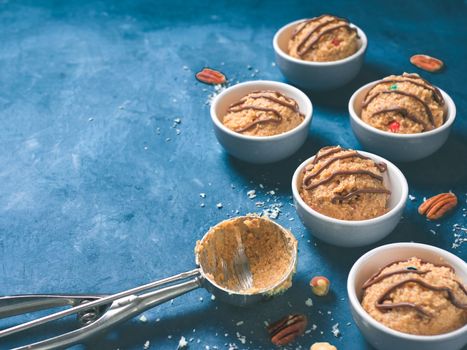 Safe-to-eat raw monster cookie dough in small portion bowl, ice cream scoop and nuts on blue background. Ideas and recipes for kids and toddlers meal. Copy space for text.