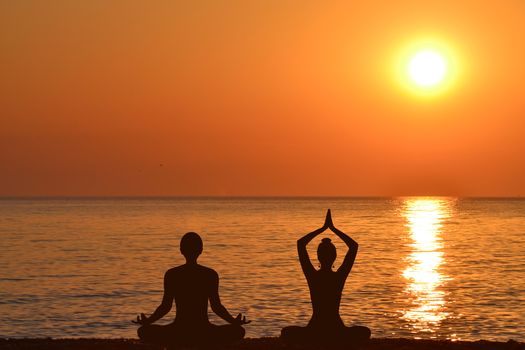 Silhouette of woman and man practicing yoga on the beach at sunrise