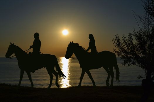Two riders riding during sunset on the seashore