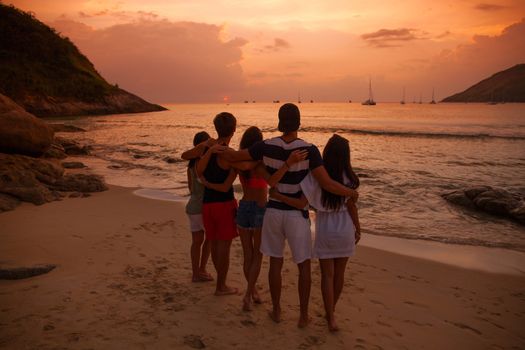 Group of happy people at sea beach at sunset