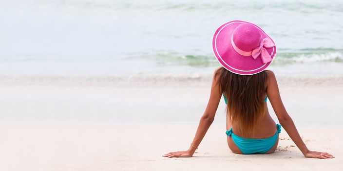 Woman in big hat sitting on beach by the sea