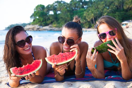 Happy smiling female friends eating watermelon on beach
