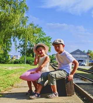 Adorable little girl and boy on a railway station, waiting for the train with vintage suitcases. Traveling, holiday and chilhood concept. Travel insurance concept. Vacation trip.