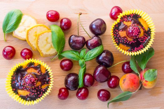 Delicious homemade cupcakes isolated on a wooden background with cherry, confectionery and chocolate sauce. served with fruit pieces. Top view.