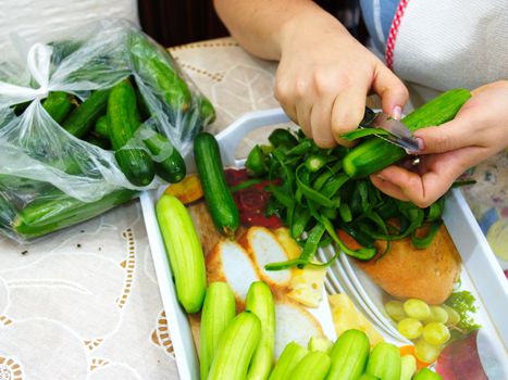 prepare a salad. cleanses cucumber shells with women's hands. cucumber is cleaned with a peeling knife. Preparing for meals