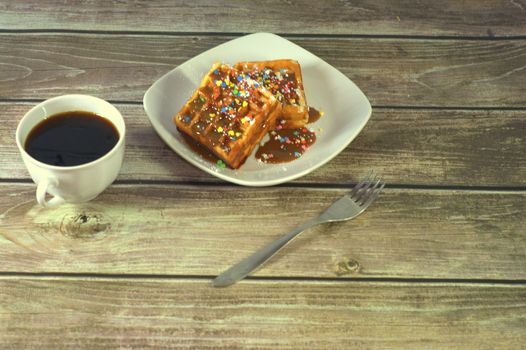 A cup of black coffee, a fork and a plate with two Viennese waffles.