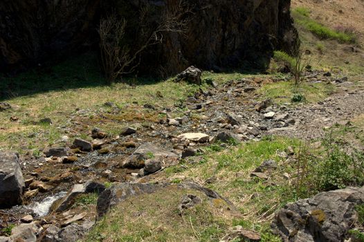 A small mountain stream flowing through a clearing surrounded by stones. Altai, Siberia, Russia.