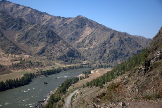 The swift turquoise river flows through the valley in the fusion of mountain ranges. Altai, Siberia, Russia.