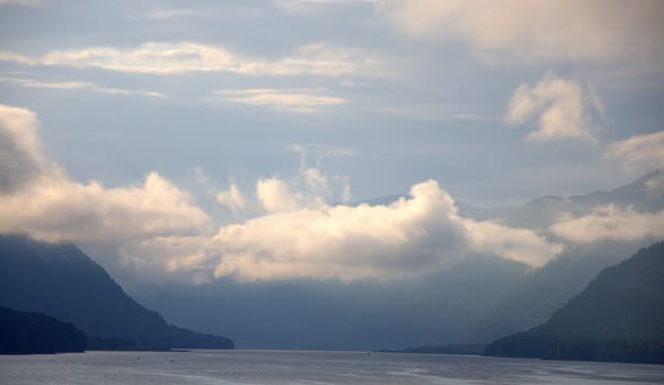 Low clouds before the rain descend from the mountains to the surface of a mountain lake. Teletskoye Lake, Altai, Siberia.