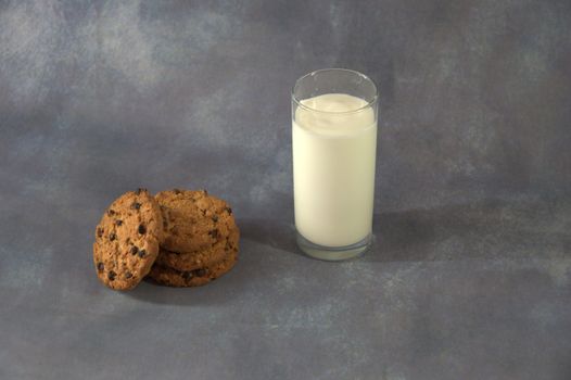 A tall glass cup with milk and a stack of oatmeal cookies with chocolate.