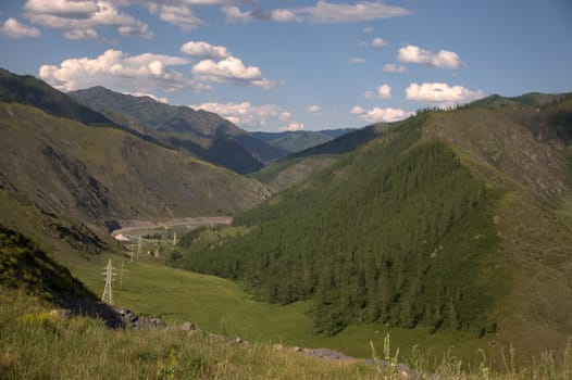 Power line posts go through a mountain valley. Altai, Siberia, Russia.