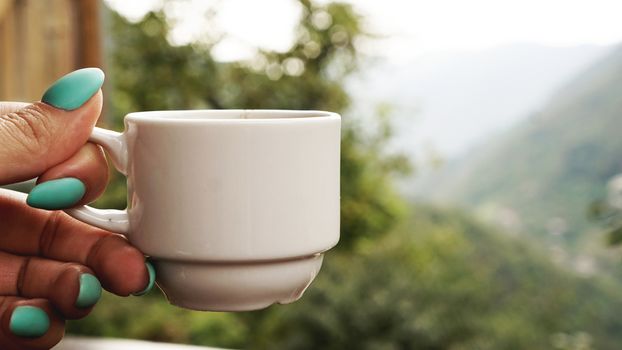 Hand white cup of hot coffee. In the morning, cold mountain views, soft focus, blurred