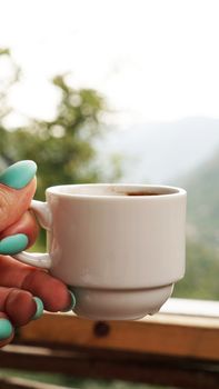 Hand white cup of hot coffee. In the morning, cold mountain views, soft focus, blurred