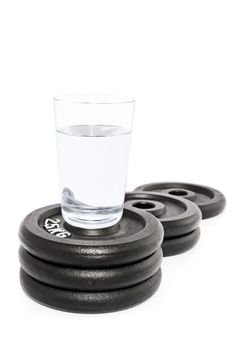 Glass of water put on a podium of weight plates, isolated on white background.