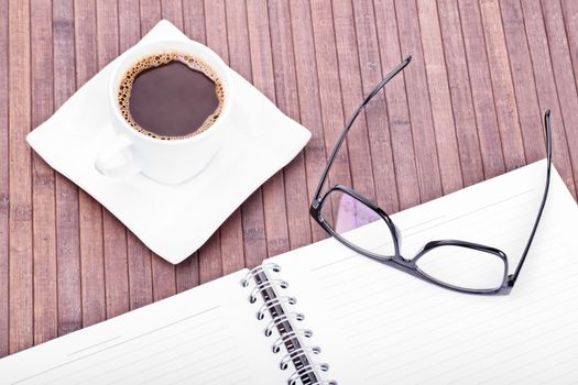 Cup of coffee with glasses and notebook on a wooden background. Time for a study break.