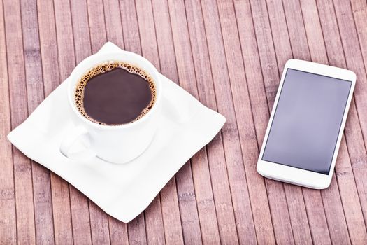Cup of coffee next to a smartphone on a wooden background.