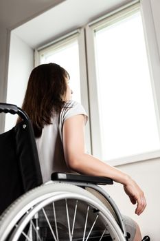 Invalid or disabled young woman person sitting wheelchair indoor looking window daylight bright sky