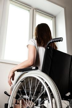 Invalid or disabled young woman person sitting wheelchair indoor looking window daylight bright sky