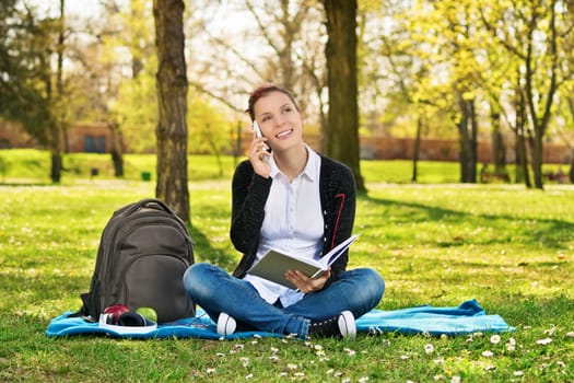 A portrait of a beautiful female student in a park with an open book, talking on the phone.