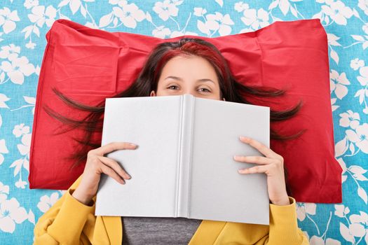 How this read makes me laugh. Young girl lying in bed, hiding her smile behind an open book.