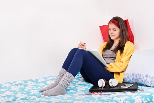 Beautiful young student girl sitting in her bedroom on her bed and writing in a notebook. Writing, studying, learning in my room.