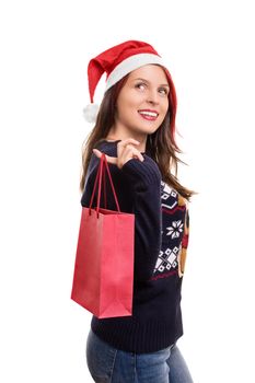 Holidays, shopping and presents. Beautiful young girl in winter clothes, wearing santa's hat, holding a shopping bag, isolated on white background.