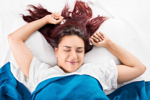 Close up of a beautiful smiling young girl waking up fresh and stretching in bed, isolated on white background.