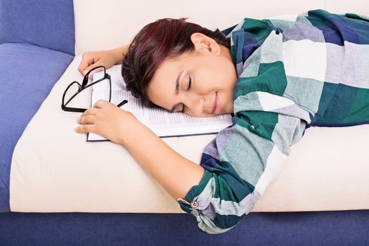 Beautiful young girl fell asleep on the couch while studying for her exams.