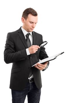 A portrait of a young businessman looking at a document on a clipboard through a magnifying glass, isolated on white background.