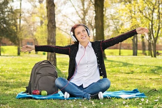 My song, my place and my freedom. Beautiful young student girl in park with arms outstretched as if she's flying while listening music.