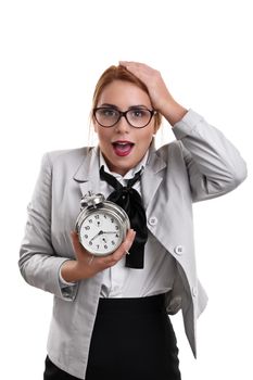 Beautiful young business woman dressed in a suit holding a clock with shocked expression, isolated on a white background.