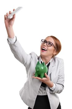 Smiling beautiful young business woman dressed in a suit with glasses taking a selfie with a green piggy bank, isolated on a white background.