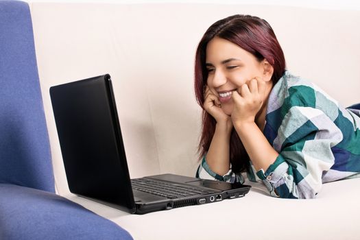 Close up shot of a beautiful smiling young girl at home lying on her couch, looking at a laptop screen. I'm happy when I talk to my favorite people.