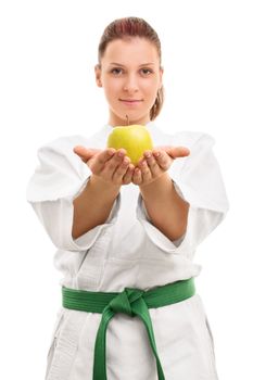Sports and healthy eating. Beautiful smiling young girl in kimono with green belt offering an apple, isolated on white background.