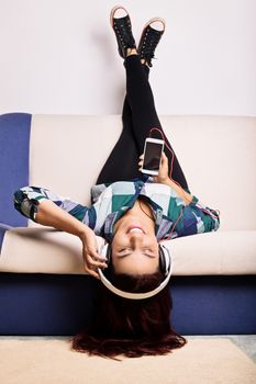 A portrait of a beautiful young girl on a sofa with her feet up, listening to her favorite music.