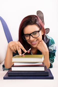 Young girl lying on a bed, playing with toy skateboard on a stack of books.