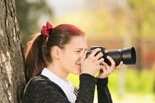 Taking photographs outdoor. Young girl in a park shooting with her professional camera.