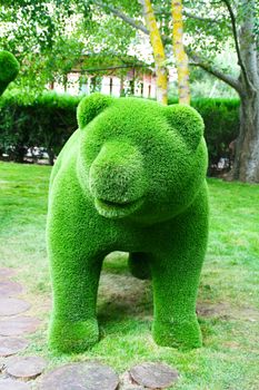 
Green bear made of artificial grass green on the background of trees.