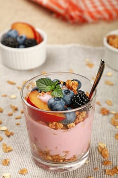 Close up portion of muesli granola breakfast with yogurt in glass, fruits and berries, high angle view