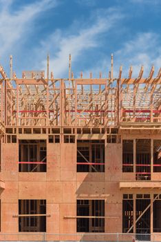 Close-up wooden framing of modern condominium building under construction in North Dallas, Texas, America. Unfinished multistory apartment complex truss, joist, beam close-up under cloud blue sky