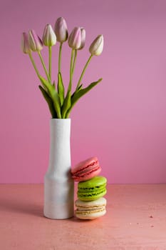 Macaroons on a pale pink background next to a vase of tulips. Place for text