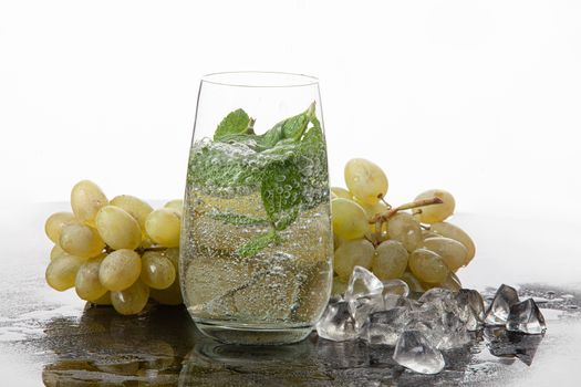 Glass of water, mint and grape on a glass background