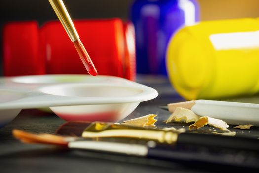 Closeup artist paint brush above color plate and poster color bottle on table. Concept of art education.