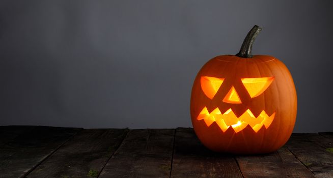 Glowing Halloween pumpkin head jack lantern on gray old wooden background
