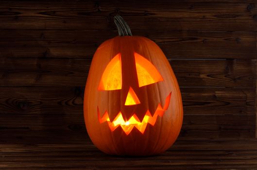 Halloween pumpkin head jack o lantern with candle inside on wooden background