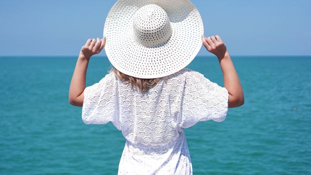 Young woman standing on sand near sea and holding a white hat